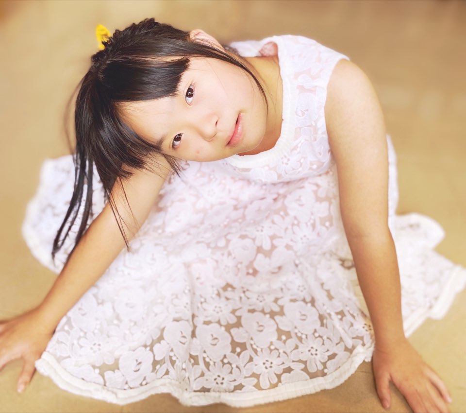 Megan Tang in a white lace dress, seated on the floor in a dance pose, 2021